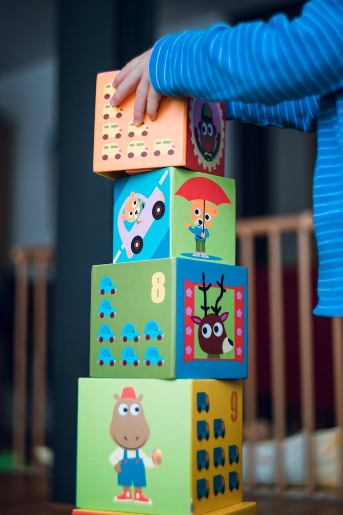Contact A child playing indoors, stacking colorful wooden toy blocks with joyful illustrations.